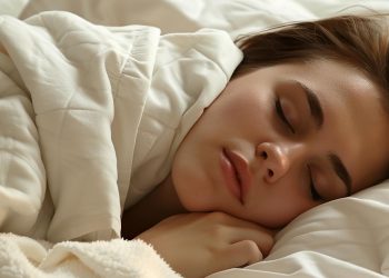 Uma pessoa dormindo pacificamente sob um cobertor branco, com a cabeça apoiada em um travesseiro. A iluminação suave lança um brilho suave na cena serena. | YogaLounge