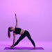 Uma pessoa faz uma pose de yoga em um tapete, estendendo um braço para cima e o outro em direção ao chão. O fundo é um gradiente de tons roxos. | YogaLounge