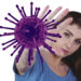 Uma mulher estende a mão para a frente como se fosse bloquear ou parar um grande vírus ilustrado em roxo, simbolizando proteção — uma imagem que evoca Como Fortalecer o Sistema Imunológico com Yoga — em um fundo branco. | YogaLounge
