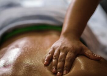 Um close-up de uma pessoa recebendo uma massagem ayurveda, mostrando uma mão pressionando suas costas oleadas. O foco é a mão e a pele relaxada e brilhante. | YogaLounge