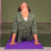 Uma pessoa com um top verde estampado pratica uma pose de ioga em um tapete roxo dentro de casa, arqueando as costas com a cabeça inclinada para cima e as mãos pressionando o tapete. | YogaLounge