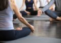 Um grupo de pessoas senta-se de pernas cruzadas em tapetes de ioga em um estúdio bem iluminado, praticando meditação com as mãos apoiadas nos joelhos, concentrando-se no relaxamento, na atenção plena e na prevenção do diabetes com ioga. | YogaLounge